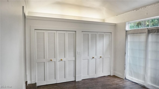 unfurnished bedroom featuring baseboards, dark wood-style flooring, and multiple closets