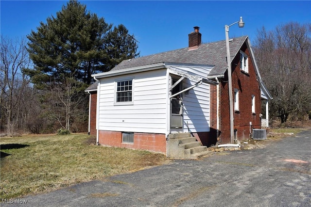 view of side of property featuring a yard, brick siding, a chimney, and central AC unit