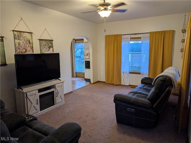 carpeted living room featuring ceiling fan, arched walkways, and baseboards