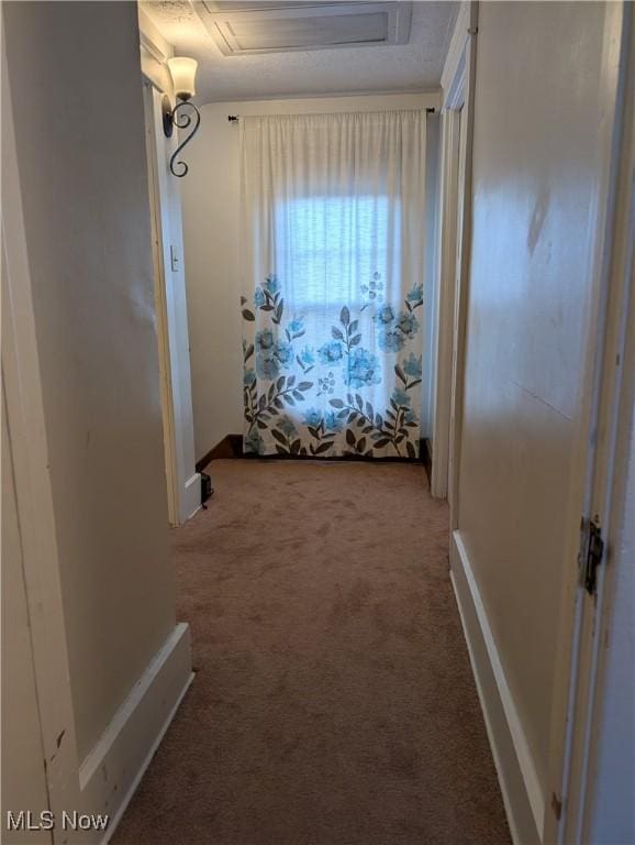 hallway featuring carpet flooring, attic access, and baseboards