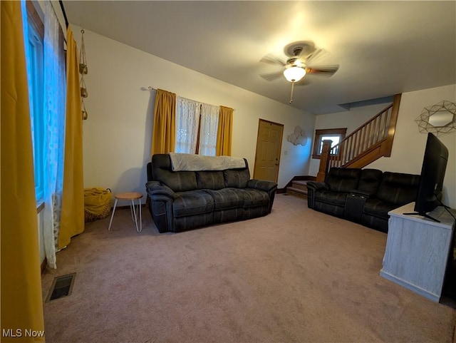 carpeted living area with stairway, ceiling fan, and visible vents