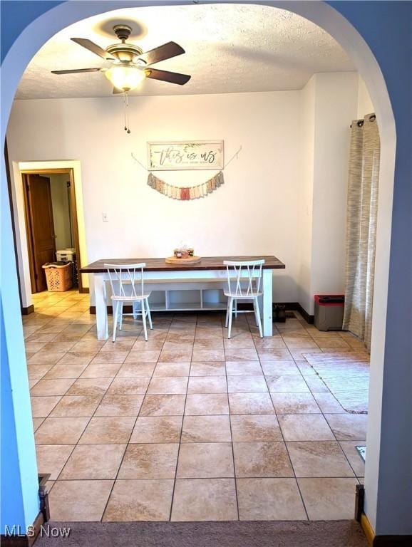 unfurnished dining area featuring a ceiling fan, arched walkways, a textured ceiling, and light tile patterned flooring