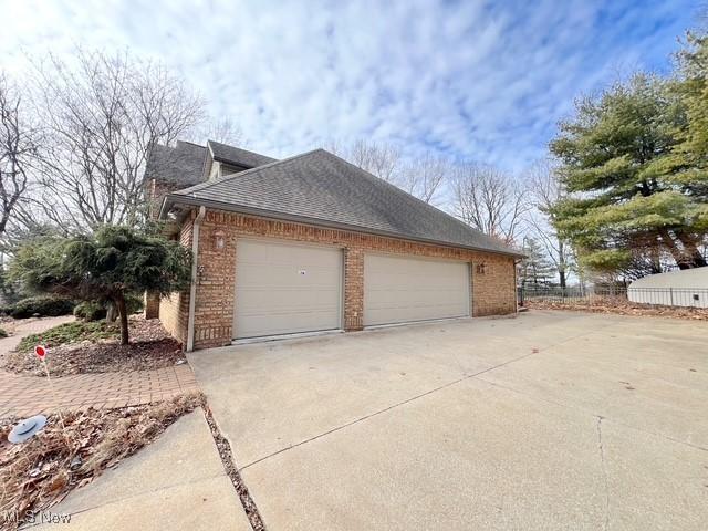 view of side of home with brick siding, a shingled roof, an attached garage, fence, and driveway