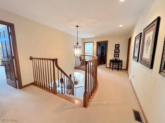 corridor featuring visible vents, baseboards, an upstairs landing, and light colored carpet