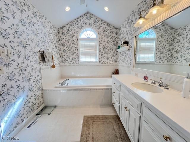 bathroom with vaulted ceiling, vanity, a bath, and wallpapered walls