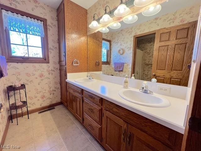 full bathroom featuring double vanity, wallpapered walls, baseboards, visible vents, and a sink