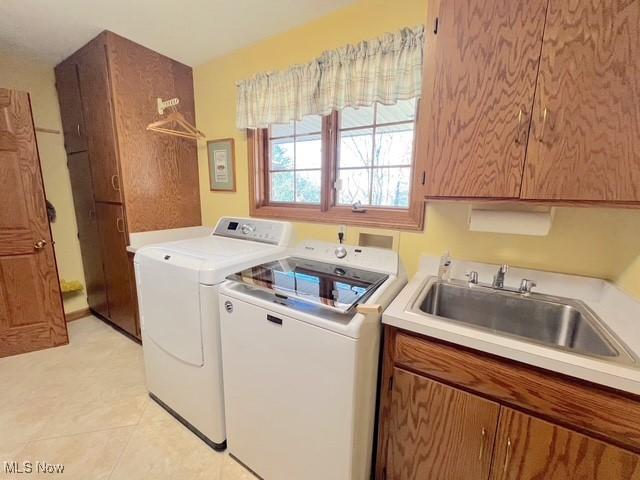 clothes washing area with light tile patterned floors, washing machine and dryer, a sink, and cabinet space