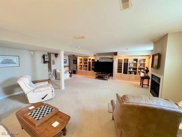 carpeted living area with a glass covered fireplace, visible vents, stairway, and baseboards