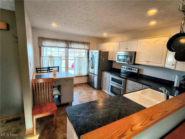 kitchen with appliances with stainless steel finishes, a sink, visible vents, and white cabinets