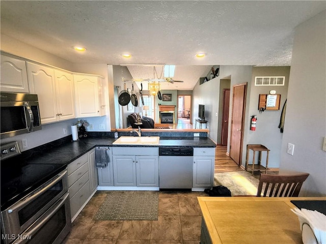 kitchen with dark countertops, visible vents, appliances with stainless steel finishes, a glass covered fireplace, and a sink