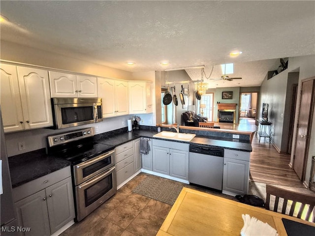 kitchen featuring a glass covered fireplace, appliances with stainless steel finishes, a peninsula, white cabinetry, and a sink