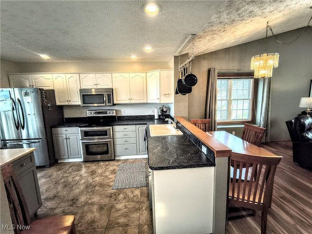 kitchen with stainless steel appliances, a peninsula, a sink, vaulted ceiling, and dark countertops