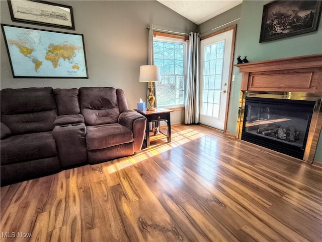 living area featuring a glass covered fireplace, vaulted ceiling, and wood finished floors