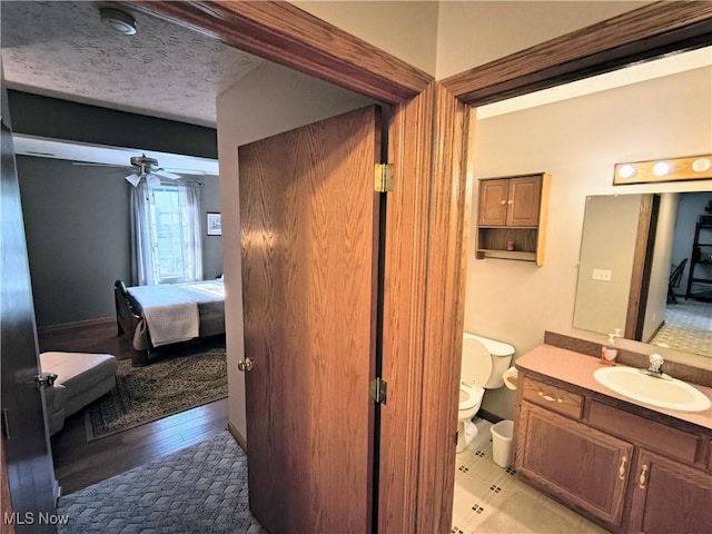 bathroom with toilet, ceiling fan, a textured ceiling, ensuite bath, and vanity