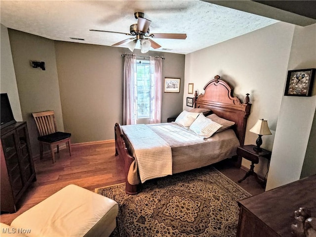 bedroom with baseboards, visible vents, a ceiling fan, wood finished floors, and a textured ceiling