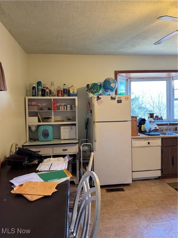 kitchen featuring ceiling fan, a textured ceiling, white appliances, a sink, and visible vents