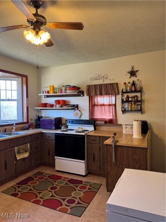 kitchen featuring light tile patterned floors, light countertops, electric range, a sink, and a textured ceiling