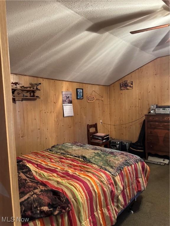 carpeted bedroom featuring wood walls, vaulted ceiling, and a textured ceiling