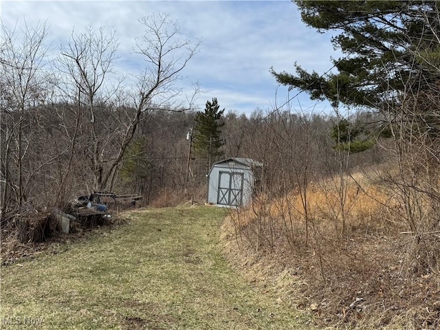 view of yard featuring an outbuilding, a view of trees, and a storage shed