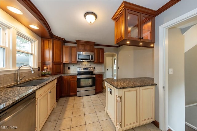 kitchen with light tile patterned floors, a sink, appliances with stainless steel finishes, cream cabinetry, and crown molding