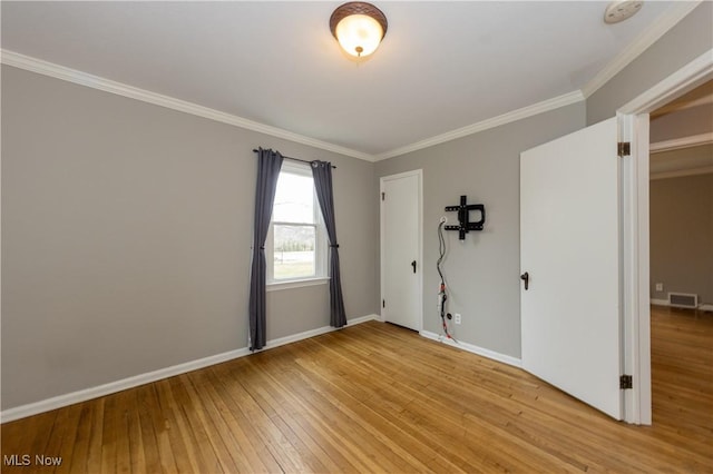 spare room featuring visible vents, ornamental molding, light wood-style flooring, and baseboards