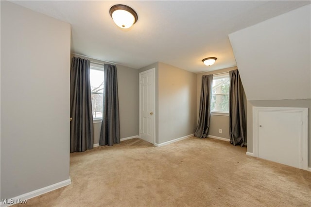 interior space with light carpet, vaulted ceiling, and baseboards