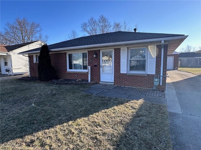 view of front of home featuring a shingled roof, a front yard, brick siding, and driveway