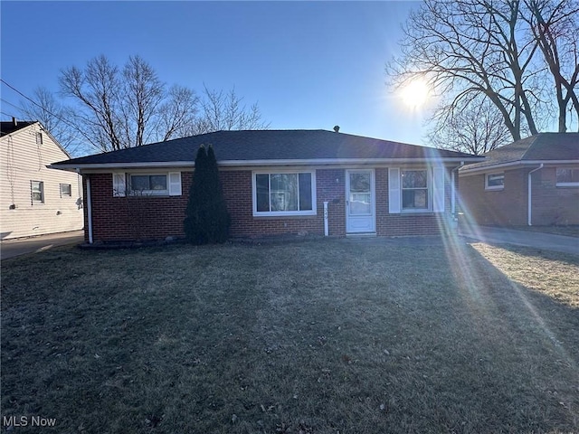 single story home featuring a front yard, brick siding, and roof with shingles