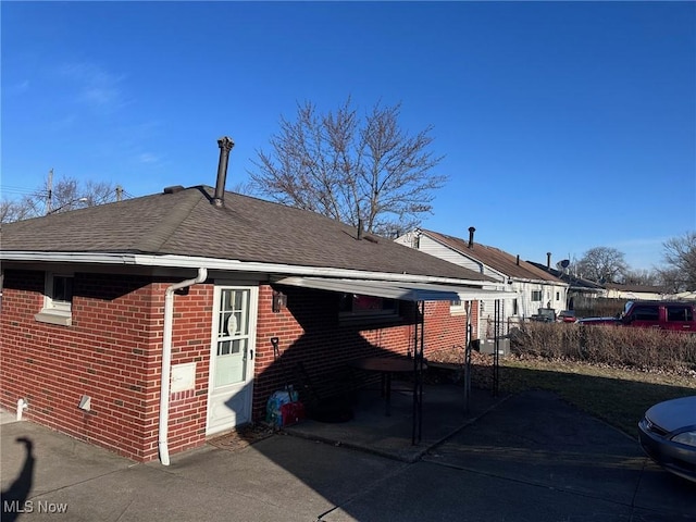 exterior space featuring brick siding and roof with shingles