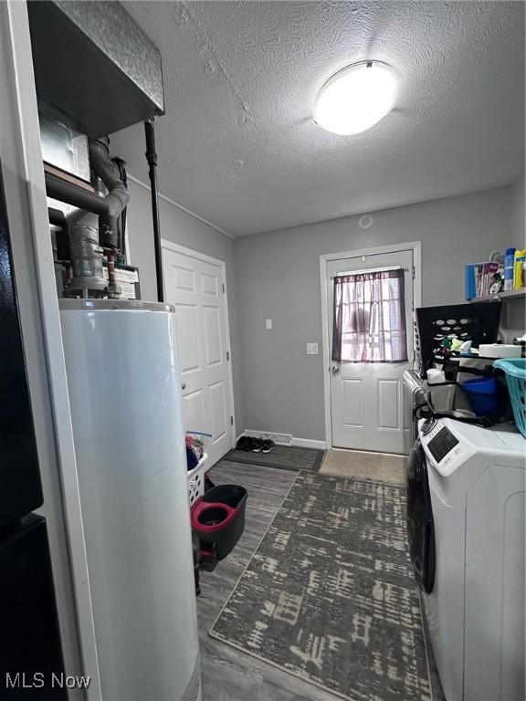 clothes washing area with laundry area, water heater, a textured ceiling, and separate washer and dryer