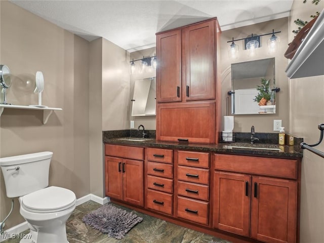 full bath featuring double vanity, a sink, toilet, and baseboards