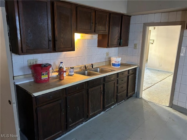 kitchen with backsplash, dark brown cabinets, a sink, and light countertops