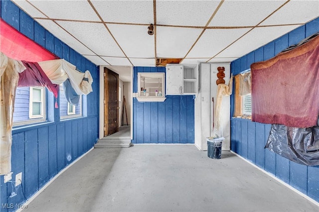 interior space featuring concrete floors, a drop ceiling, and wooden walls