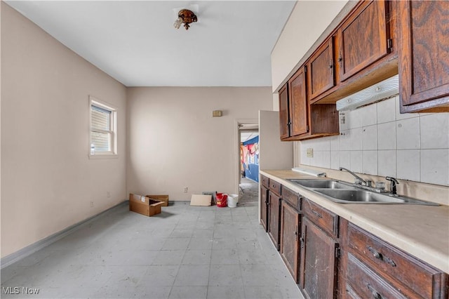 kitchen with decorative backsplash, baseboards, light countertops, and a sink