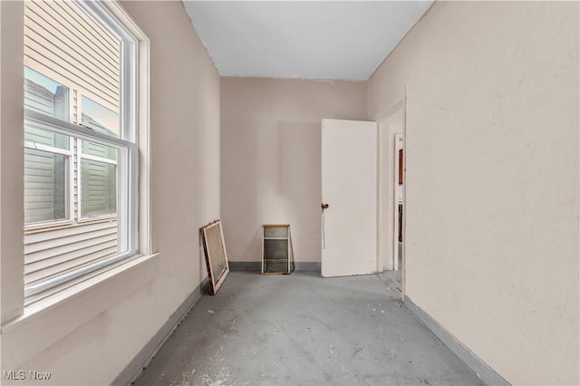 spare room featuring unfinished concrete flooring, baseboards, and a healthy amount of sunlight