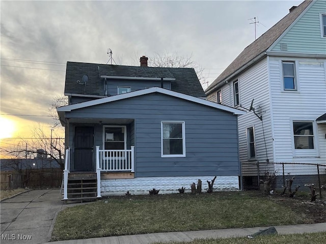 view of front of house with covered porch, a yard, a chimney, and fence