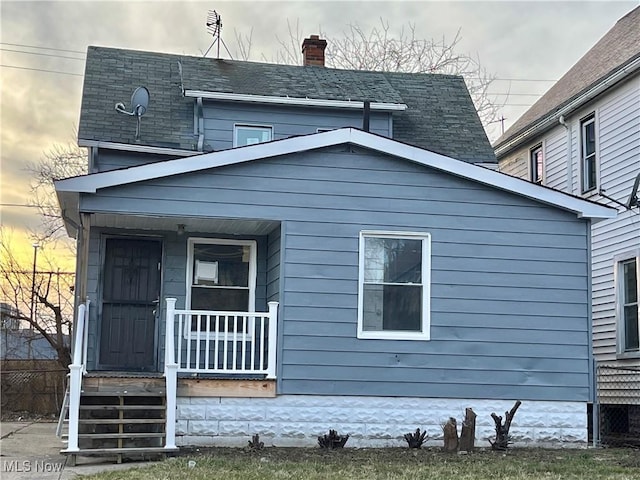 exterior space with covered porch, a chimney, and roof with shingles