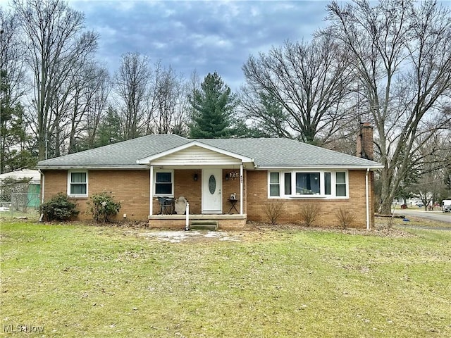 ranch-style house featuring covered porch, a chimney, brick siding, and a front yard