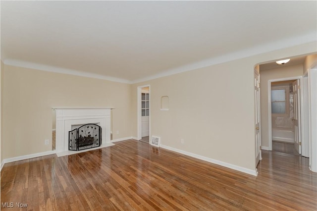 unfurnished living room with baseboards, visible vents, arched walkways, wood finished floors, and a fireplace