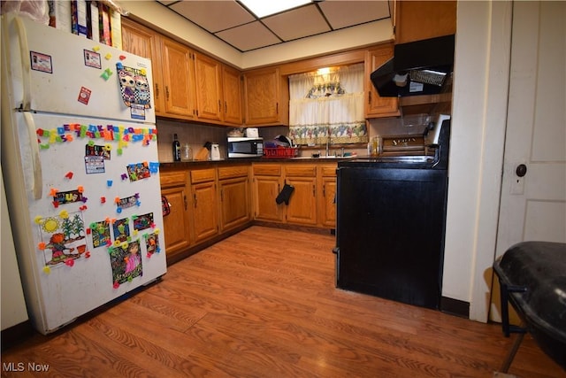 kitchen with dark countertops, stove, stainless steel microwave, freestanding refrigerator, and under cabinet range hood