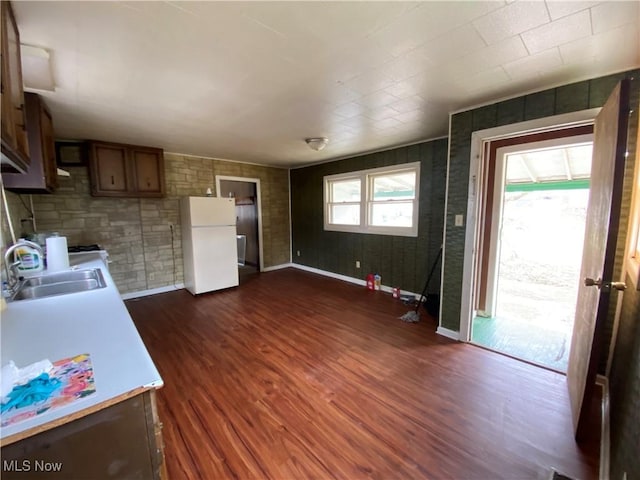 kitchen featuring baseboards, dark wood finished floors, freestanding refrigerator, light countertops, and a sink