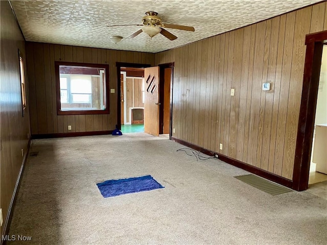 carpeted spare room with a textured ceiling, wood walls, a ceiling fan, and baseboards