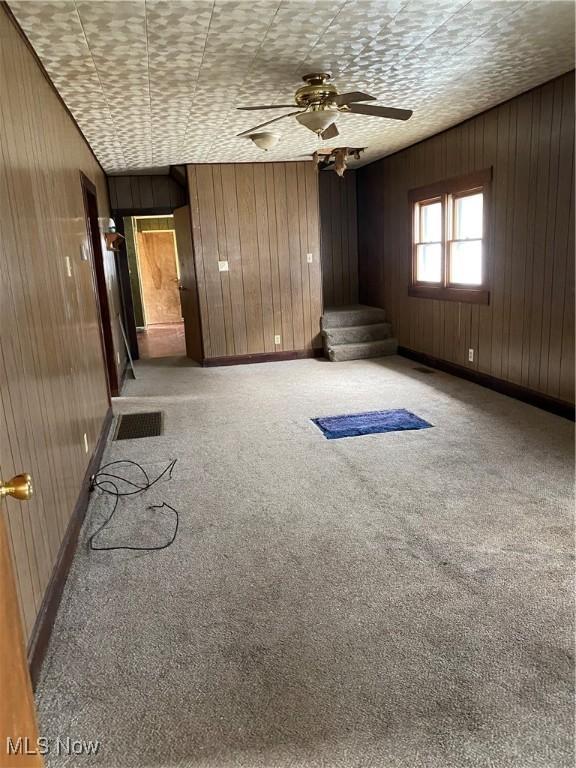 carpeted spare room featuring wood walls, baseboards, and a ceiling fan