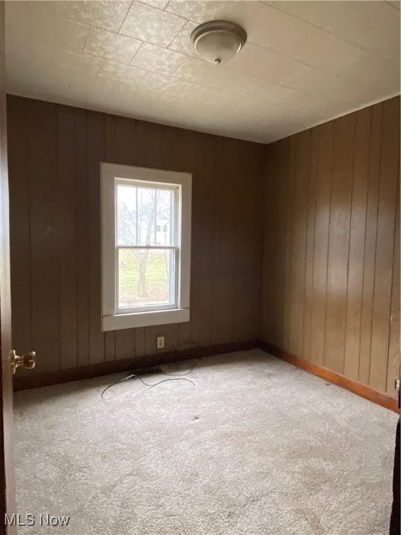 unfurnished room featuring carpet flooring, wooden walls, and baseboards