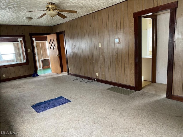 empty room featuring a textured ceiling, carpet flooring, a ceiling fan, and wooden walls