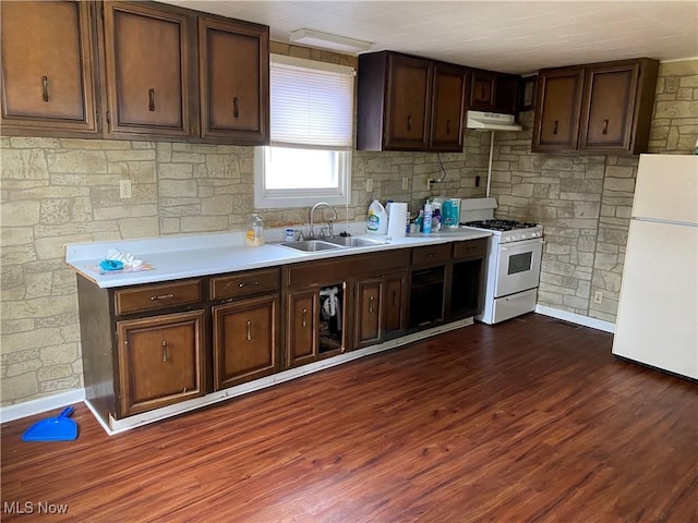 kitchen with under cabinet range hood, white appliances, dark wood-style flooring, a sink, and light countertops