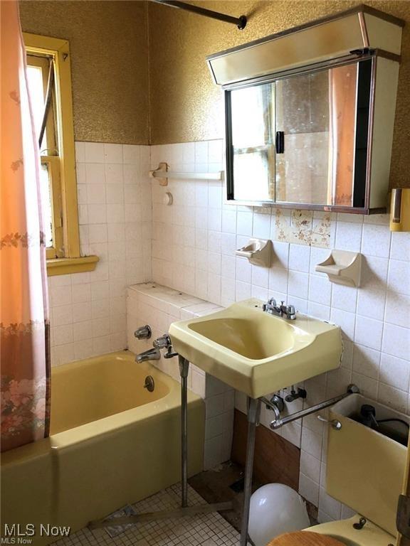 full bath featuring a sink, tile patterned flooring, tile walls, and a textured wall