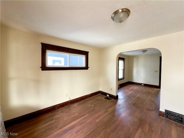 spare room with dark wood-style floors, baseboards, visible vents, and arched walkways