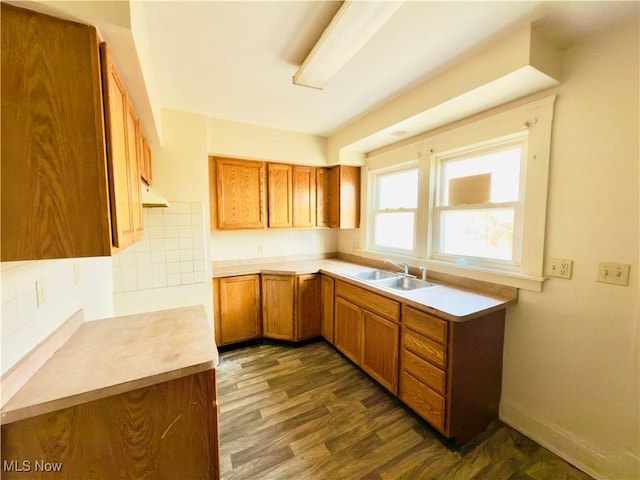 kitchen featuring dark wood-type flooring, brown cabinets, a sink, and backsplash