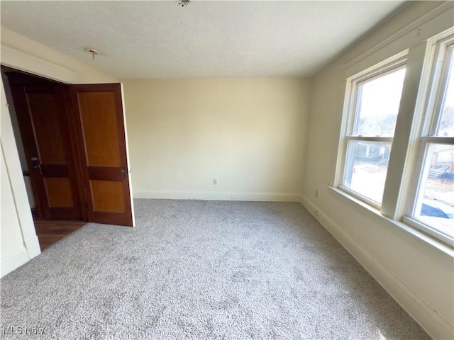 spare room with a textured ceiling, carpet flooring, and baseboards